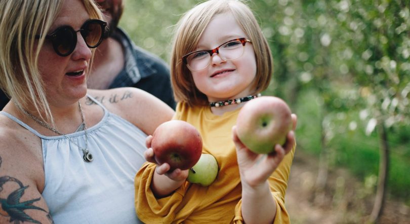 a gender diverse kid and parent holding some apples